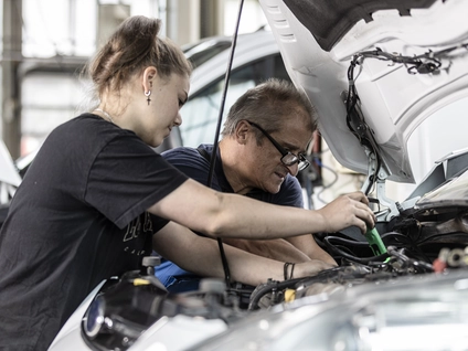 Mechanikerin und ihr Kollege bei der Arbeit an einem Auto in der Werkstatt